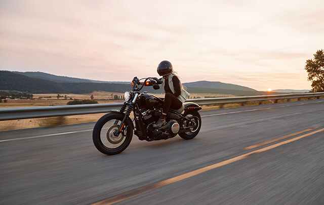 Woman right motorcycle down highway with beautiful mountains and sunset the background.