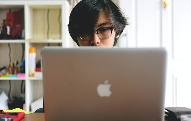 Asian man sitting behind Apple Laptop only his nose and above are visible.