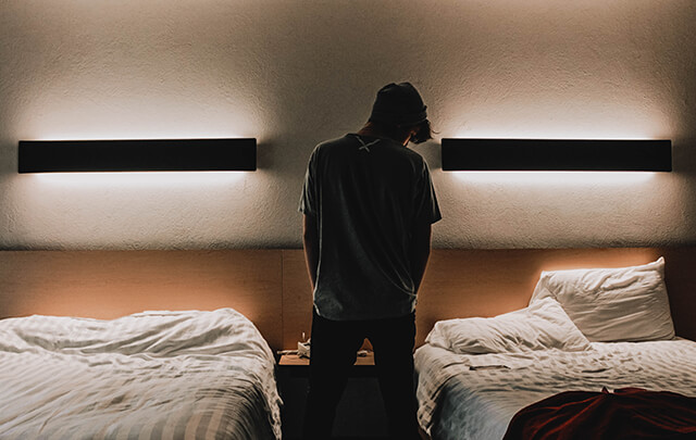 Young man standing in his bedroom at impatient rehab treatment.  Between two main beds with dramatic dim lighting on the wall